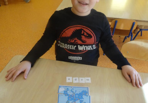 Chłopiec układa przy stoliku obrazki z części oraz rozsypankę literową.